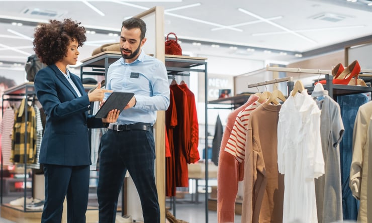 Two brick-and-mortar retail employees work on assortment planning on a tablet. 